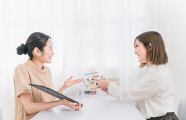 ネイルサロンでタブレットとネイルチップを見ながらネイリストにカウンセリングを受ける日本人女性
