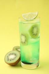 Glass of refreshing drink and cut kiwi on yellow background