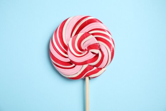 Stick with colorful lollipop swirl on light blue background, top view