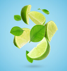 Fresh lime slices and green leaves falling on light blue background