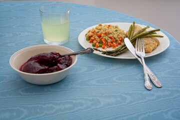 Baked  chicken breast dinner dressed with asparagus spears rice mixed with diced carrot peas cranberry sauce margarita drink