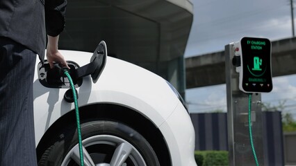 Businesswoman recharge her electric car from charging station at city center or public parking car....