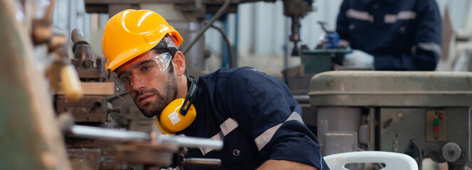 Young caucasian engineer man operating lathe machine for preparing production at factory industrial, technician or labor maintenance machinery at workplace, metalworker working, industry concept.