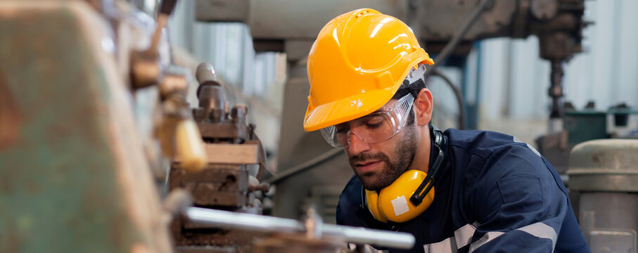 Young caucasian engineer man operating lathe machine for preparing production at factory industrial, technician or labor maintenance machinery at workplace, metalworker working, industry concept.