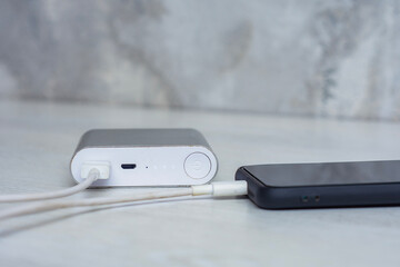 The smartphone is being charged using a portable charger on a wooden table.