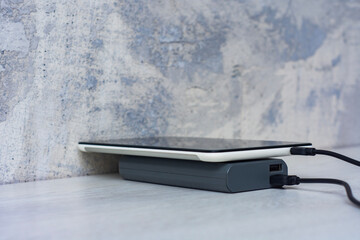 Tablet charging with power bank on a gray wooden table. Portable charger for charging devices.