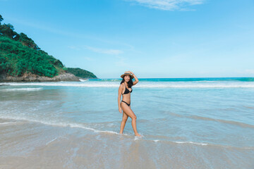 With a carefree spirit, a woman in a bikini takes a leisurely stroll on the sandy beach, fully...