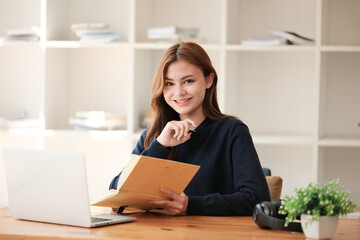 A beautiful caucasian female student is studying remotely. She is sitting at a table at home with a laptop and a notepad and concentrated is watching a video conference, Thinking.