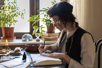 Focused illustrator artist young woman draws in notebook in cozy workshop for freelance order....