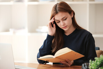 Thinking, A beautiful caucasian female student is studying remotely. She is sitting at a table at home with a laptop and a notepad and concentrated is watching a video conference.