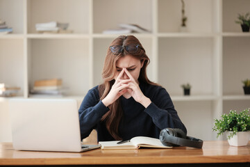 Stressed, A beautiful caucasian female student is studying remotely. She is sitting at a table at home with a laptop and a notepad and concentrated is watching a video conference lesson.