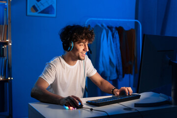 Happy young arabic gamer wearing headphones playing video game on personal computer, play in eSport...