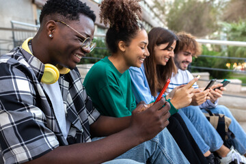 Group of happy multiracial teenage college friend students ignoring each other looking at mobile phone. Phone addiction. - obrazy, fototapety, plakaty
