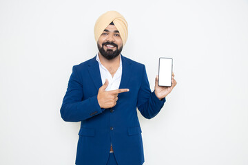 Happy young indian sikh businessman wearing suit pointing at smart phone with blank display screen...