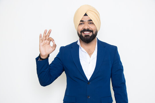 Happy young indian sikh businessman wearing suit do Ok gesture with hand isolated over white background. Corporate Concept.