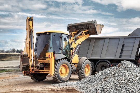 A universal loader or excavator loads sand or grain into a dump truck. Powerful modern equipment for earthworks and moving bulk cargo.