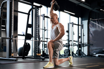 Middle aged athlete exercising kettlebell drills in gym.