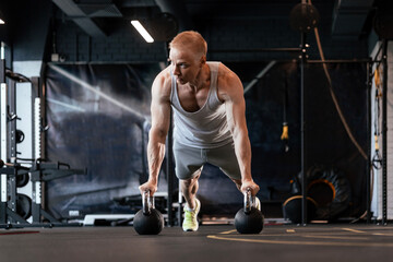 Fototapeta na wymiar Fit and muscular man doing horizontal push-ups on dumbbells in gym.