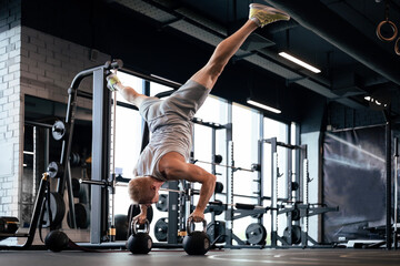 Fit and muscular man doing vertical push-ups on dumbbells in gym.