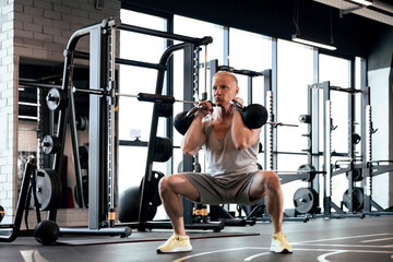 Fototapeta na wymiar Squats with kettlebells exercise. Middle aged athlete doing functional workout at the gym.