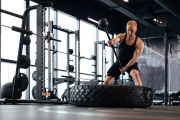 Fototapeta premium Sport training for endurance, strong man hitting hammer. Concept of crossfit workouts.