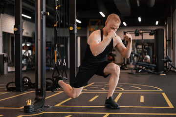 Strong sportsman doing bulgarian lunges in a gym with TRX.