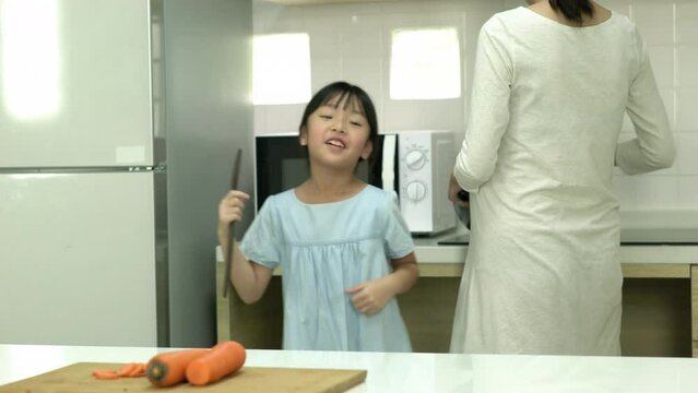 Asian family dancing and having good time in the kitchen together at home. Daughter happy cheerful with father and mother. Concept of happy family and activity holiday.
