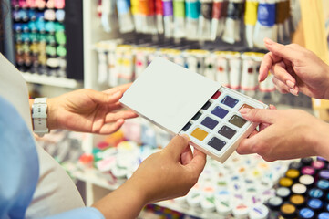 Close-up watercolor palette in hands of a seller in school stationery or art shop. Painting....