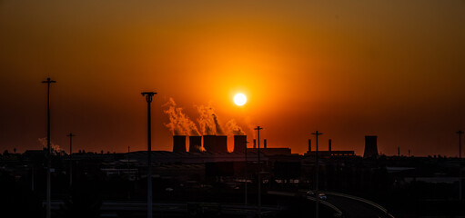 A coal fired power station contributing to pollution before sunset with light poles in foreground