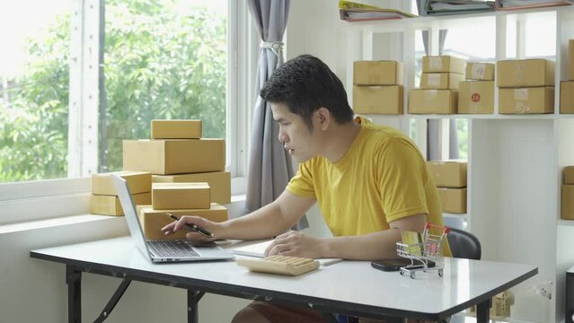 Asian young man selling online at home with box and laptop taking orders from customers, concept with SME business