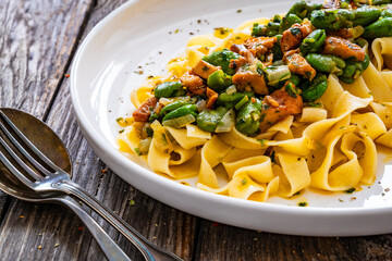 Tagliatelle with broad bean and chanterelle mushrooms on wooden table
