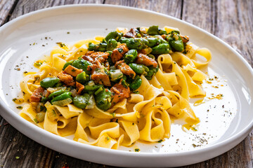 Tagliatelle with broad bean and chanterelle mushrooms on wooden table
