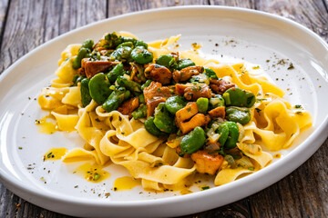 Tagliatelle with broad bean and chanterelle mushrooms on wooden table
