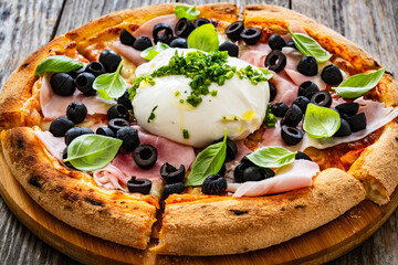 Circle prosciutto burrata pizza with black olives on wooden table
