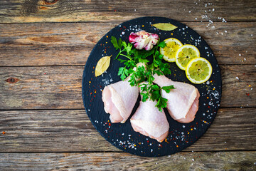 Top-down shoot of raw chicken drumsticks on cutting board with seasonings on wooden table
