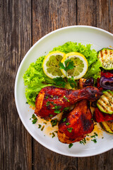 Roasted chicken drumsticks with lettuce and grilled sliced vegetables on wooden table
