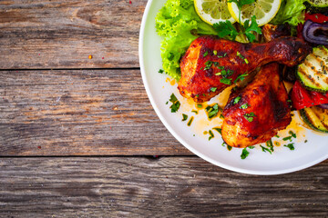 Roasted chicken drumsticks with lettuce and grilled sliced vegetables on wooden table
