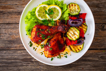 Roasted chicken drumsticks with lettuce and grilled sliced vegetables on wooden table
