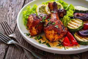 Roasted chicken drumsticks with lettuce and grilled sliced vegetables on wooden table
