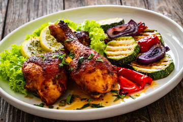 Roasted chicken drumsticks with lettuce and grilled sliced vegetables on wooden table
