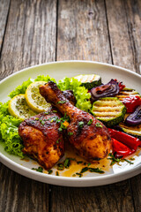 Roasted chicken drumsticks with lettuce and grilled sliced vegetables on wooden table
