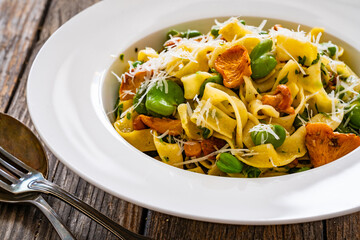 Tagliatelle with broad bean, chanterelle mushrooms and parmesan cheese on wooden table  © Jacek Chabraszewski