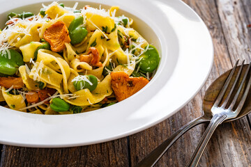 Tagliatelle with broad bean, chanterelle mushrooms and parmesan cheese on wooden table
