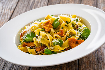 Tagliatelle with broad bean, chanterelle mushrooms and parmesan cheese on wooden table

