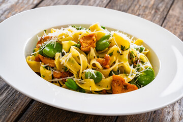 Tagliatelle with broad bean, chanterelle mushrooms and parmesan cheese on wooden table
