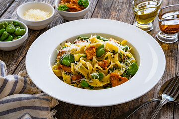 Tagliatelle with broad bean, chanterelle mushrooms and parmesan cheese on wooden table
