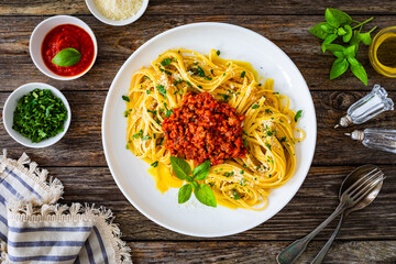 Top-down shoot of linguine with minced pork meat in tomato sauce  with parmesan cheese and basil leaves served on wooden table
