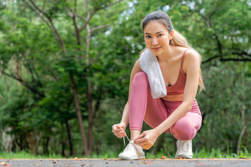 Young attractive Asian woman tying her shoelace before her morning exercise run at running track of...