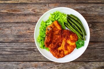 Breaded fried pork chop with cooked green beans on wooden table
