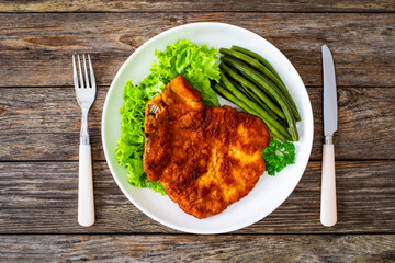 Breaded fried pork chop with cooked green beans on wooden table
